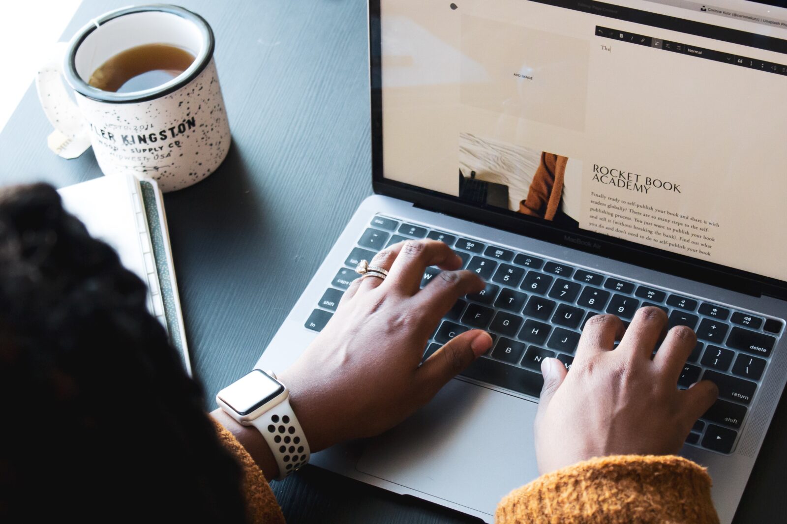 person bloggin on computer with tea cup sitting next to them